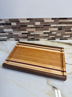 Heritage Cutting Board 18” × 12” × 1.5” — Maple, Walnut, Cherry & Purple Heart | Juice Groove + Hand Holds with brass feet