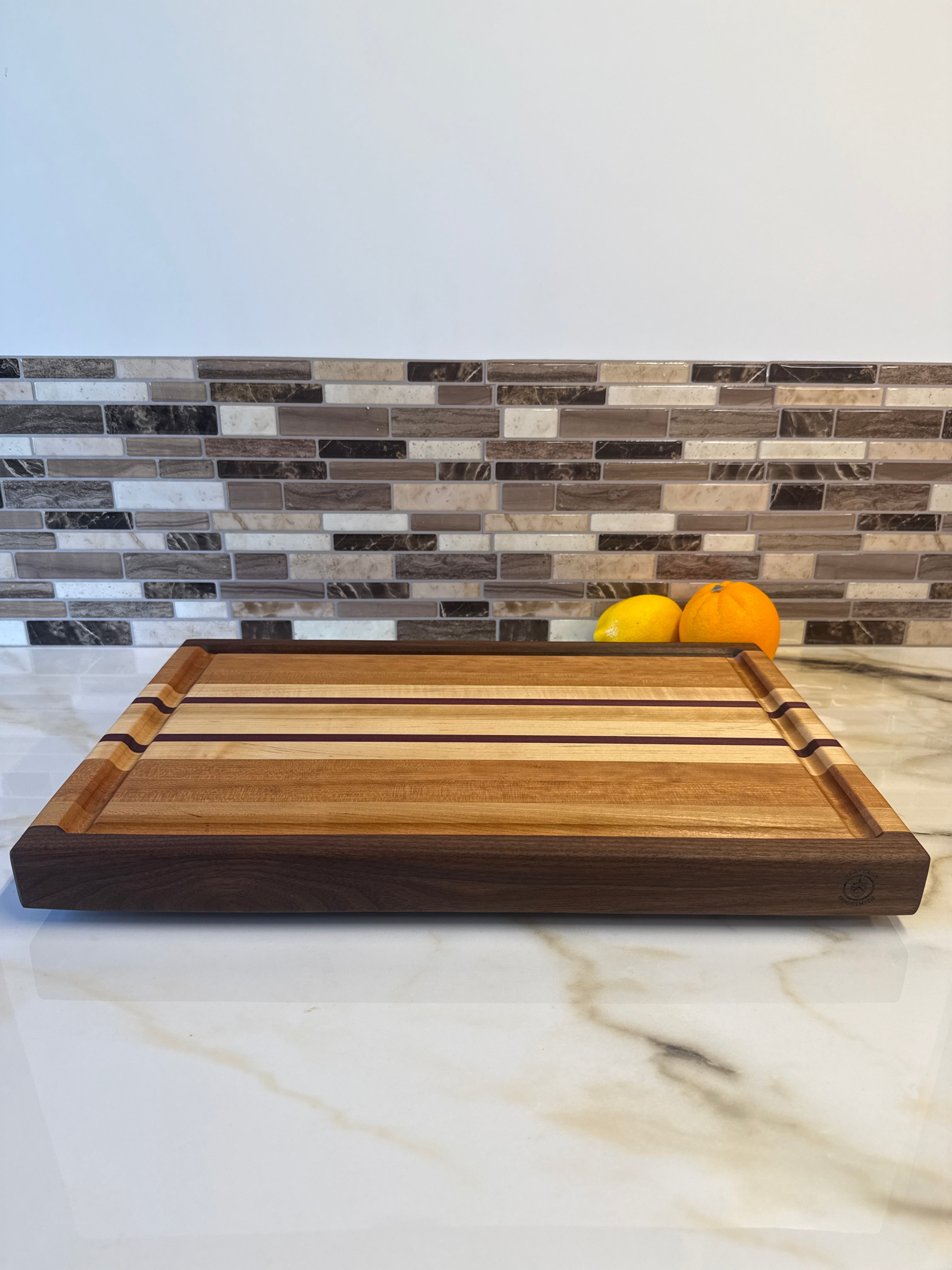 Heritage Cutting Board 18” × 12” × 1.5” — Maple, Walnut, Cherry & Purple Heart | Juice Groove + Hand Holds with brass feet
